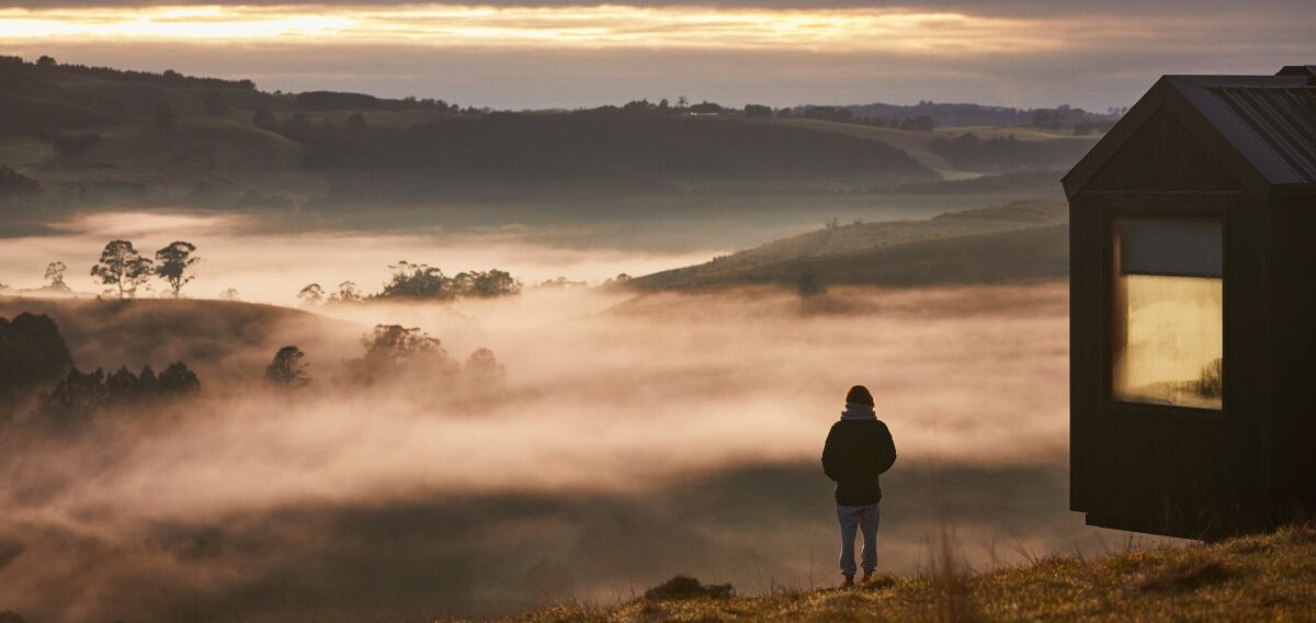 Person standing beside a Unyoked cabin overlooking misty hills at sunrise