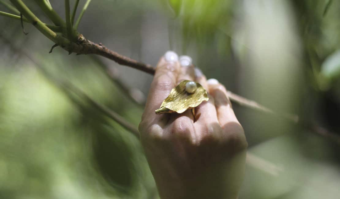 Gold leaf-shaped ring on hand, background is green trees