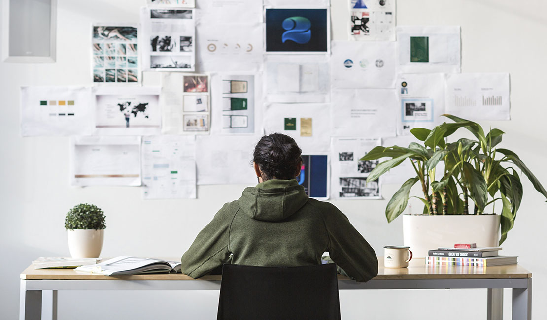 person in ponytail sitting at desk with vision board on wall