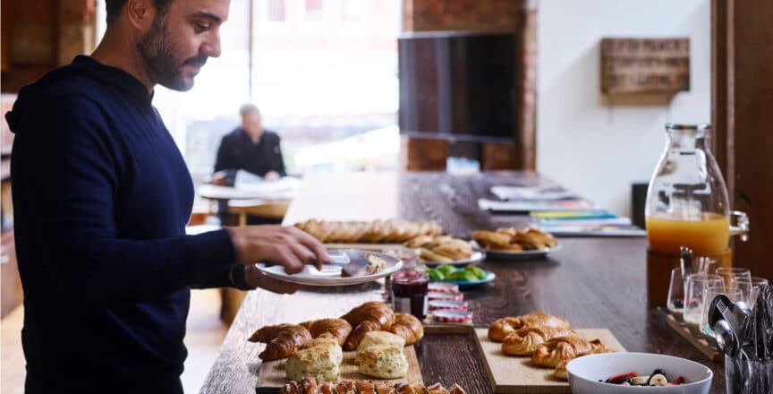 man serving himself from a breakfast buffet in an office kitchen