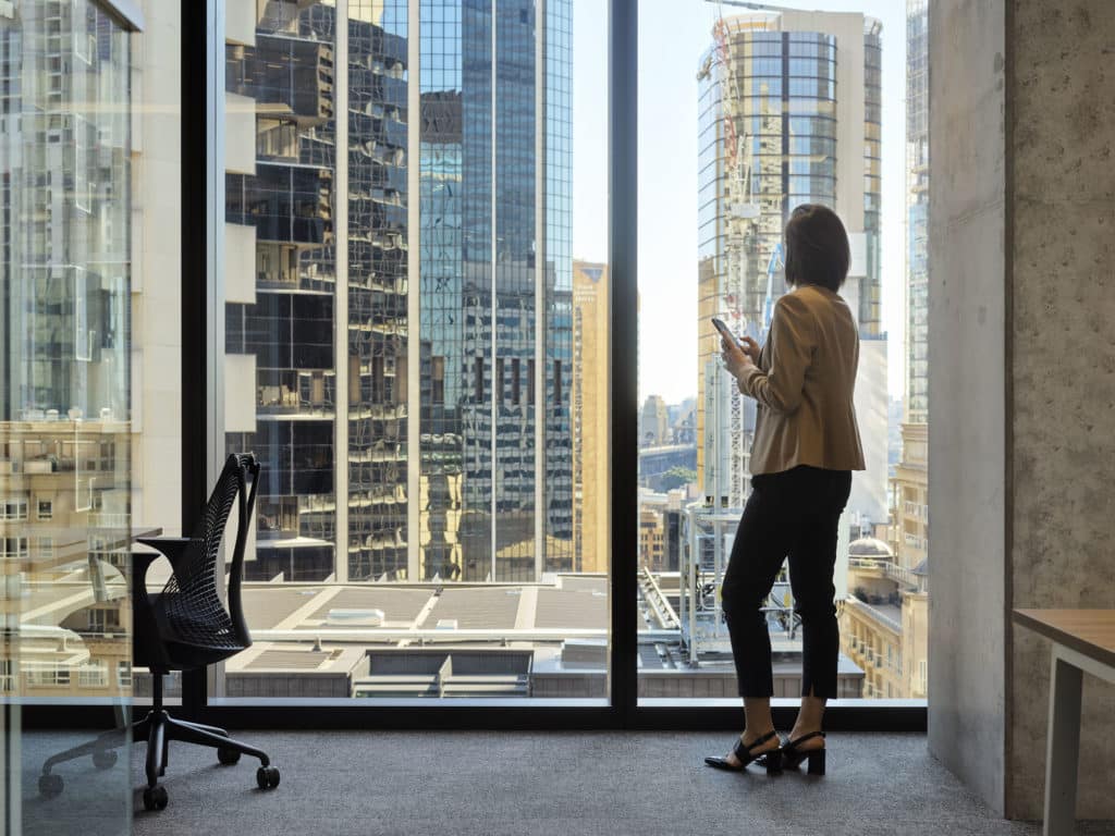 woman staring out city window with phone in hand