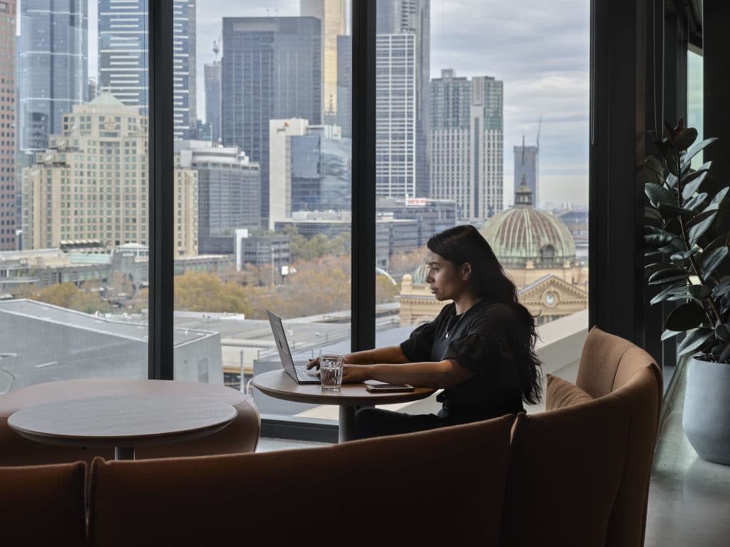 woman working on laptop with a view of Flinders Street Station in the background as seen from Hub Flinders Street office space