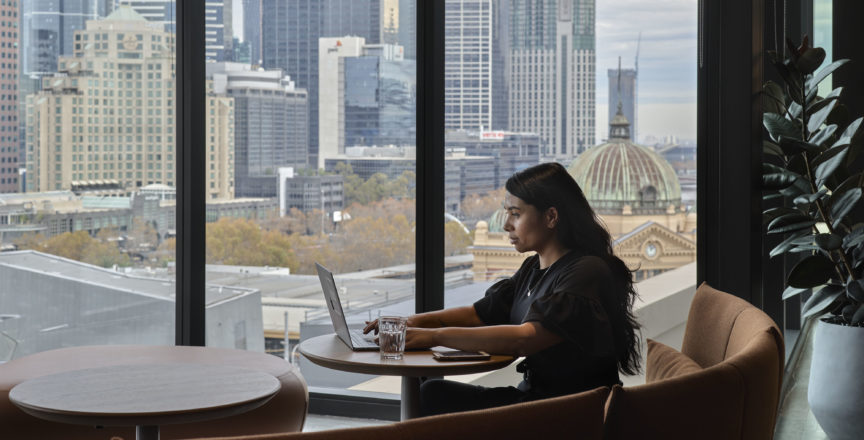 woman working on laptop with a view of Flinders Street Station in the background as seen from Hub Flinders Street office space