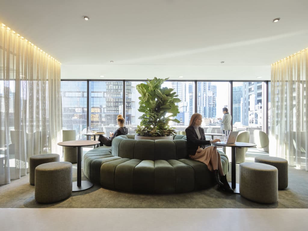 A beautiful circular green couch with people sitting around it working.