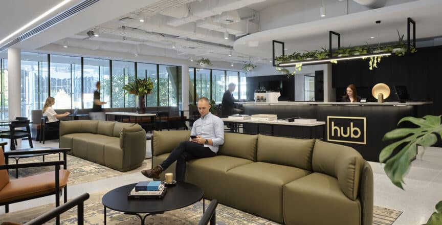 man sitting on a green couch reading a book with a welcome desk behind him