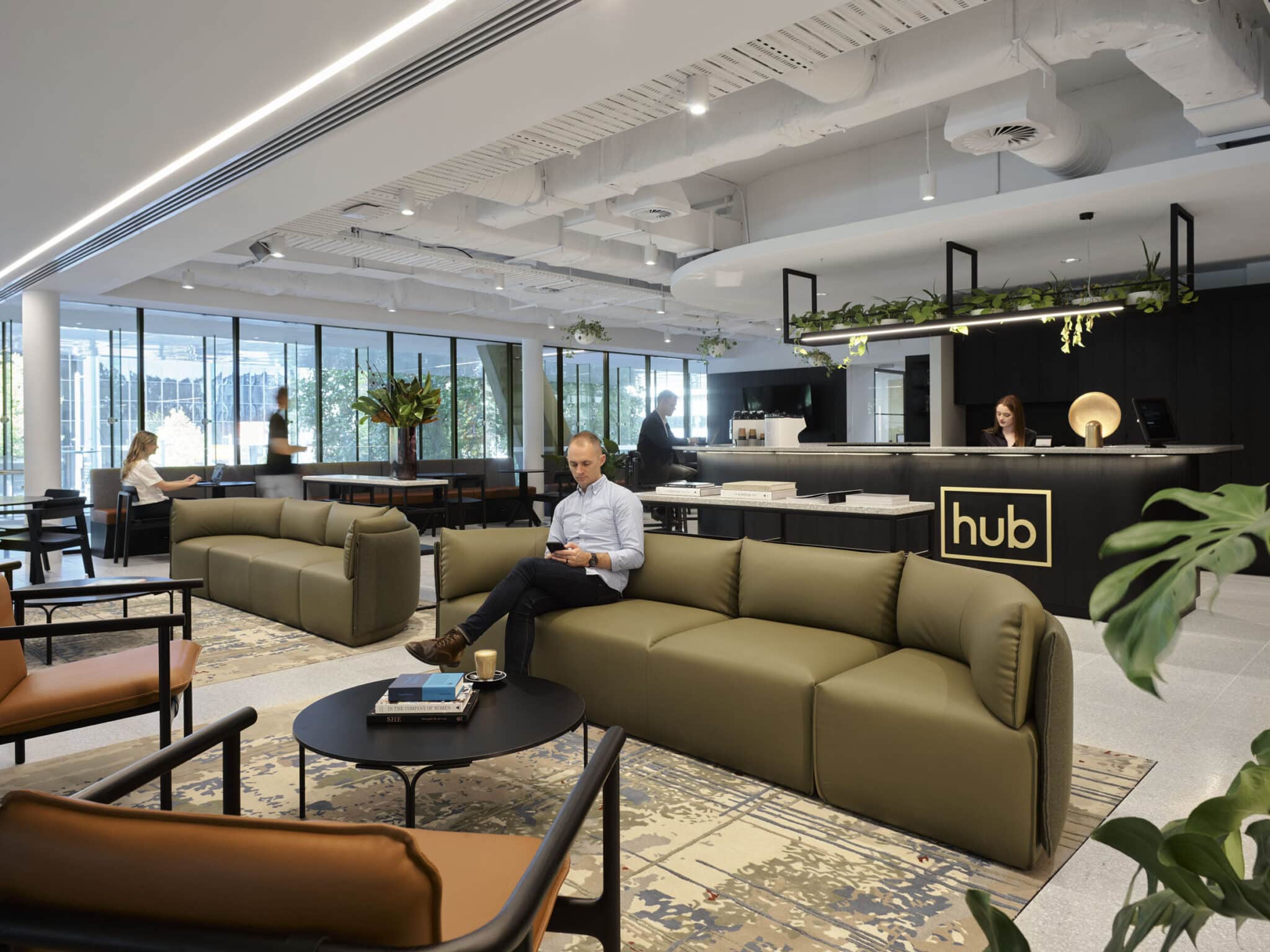 man sitting on a green couch reading a book with a welcome desk behind him