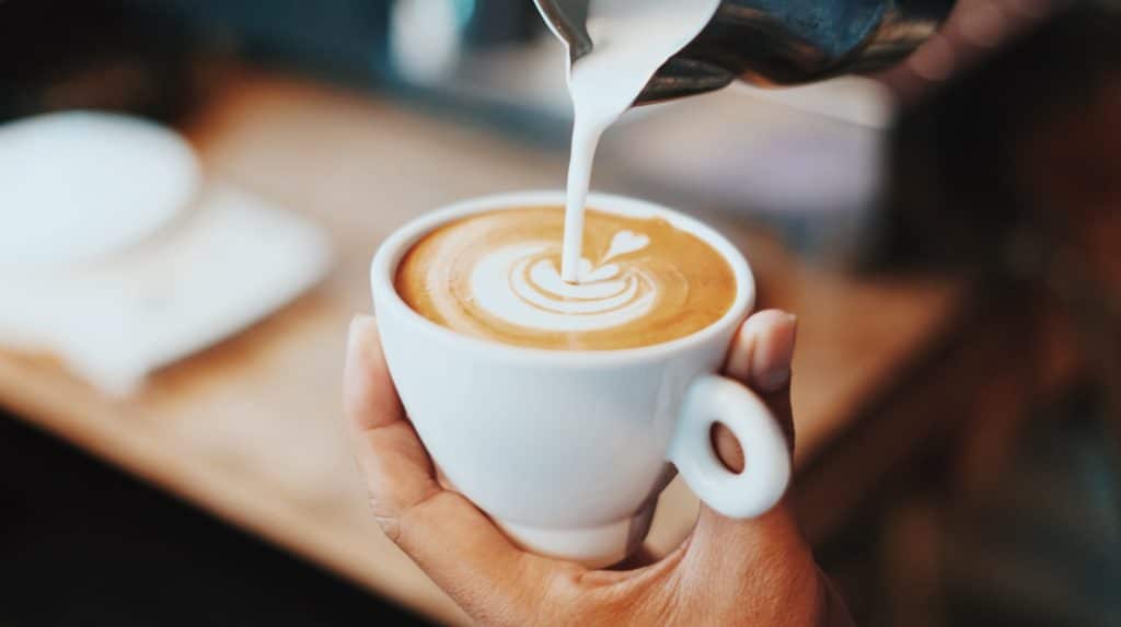person pouring milk into a coffee mug barrista made