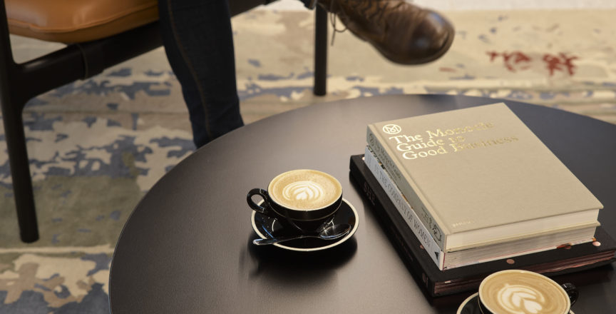 a person sitting at a table with two coffees and a book