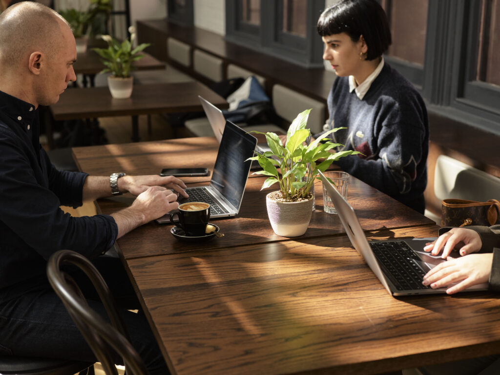 people working at a desk in cafe with plants in