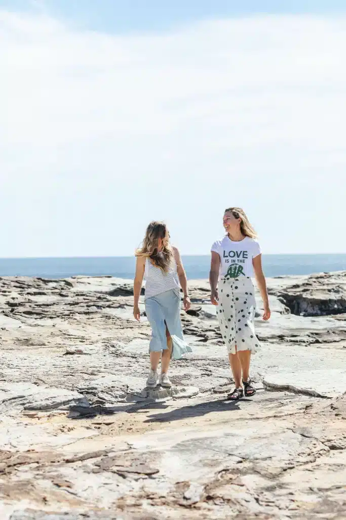 Two women standing on the rocks at a beachhe r