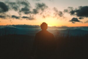 man sitting looking at sunset on hill