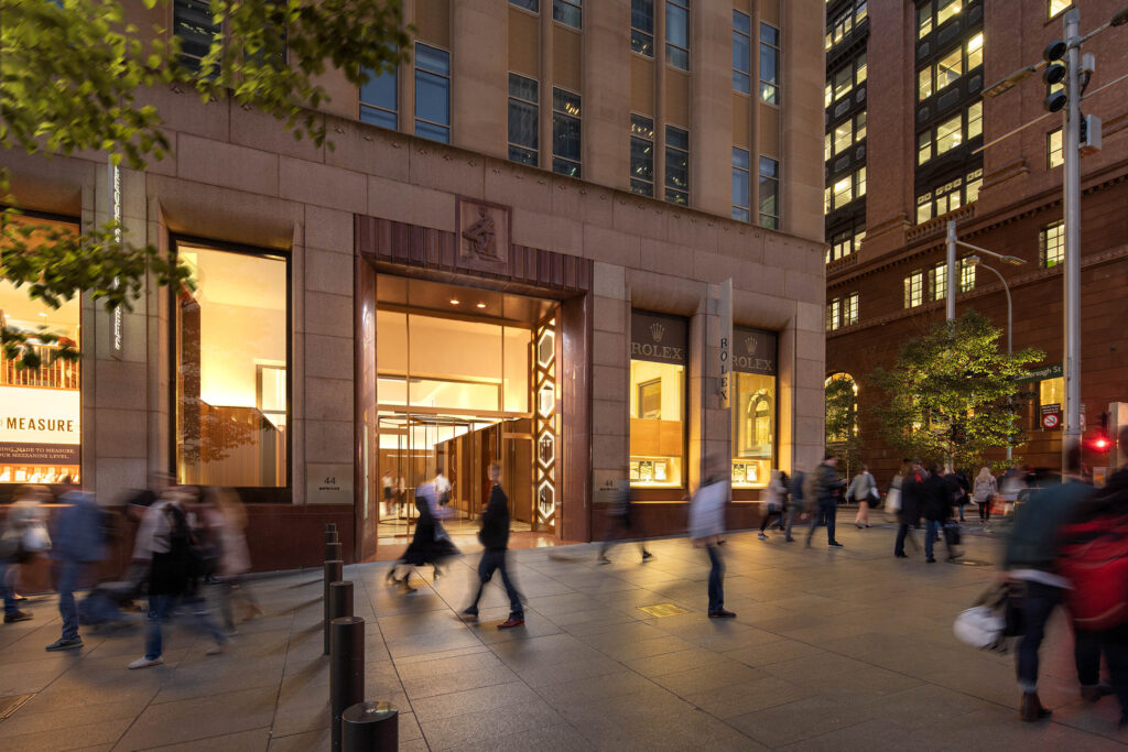 An image of the Rolex Boutique in Martin Place. The lights are on and there are people walking around outside.