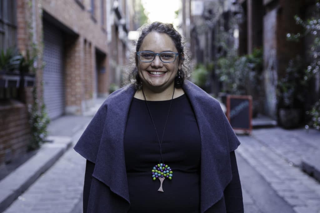 woman in dark clothing standing on road, smiling into the camera