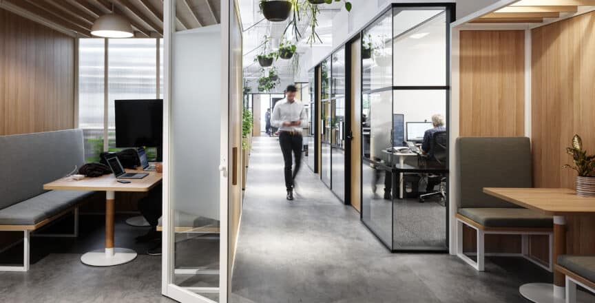a man walking down the corridor of a workspace. There are seats on either side of him.