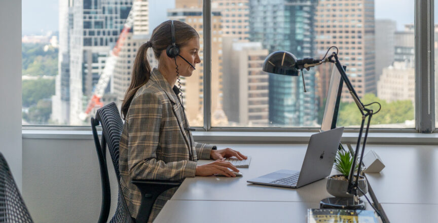 A woman sitting at a desk infront a computer with a headset on