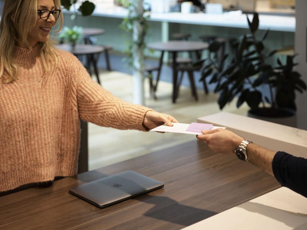 A lady at a concierge desk is handing over an envelope to a customer