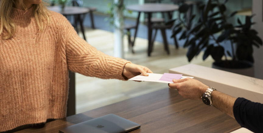 A lady at a concierge desk is handing over an envelope to a customer