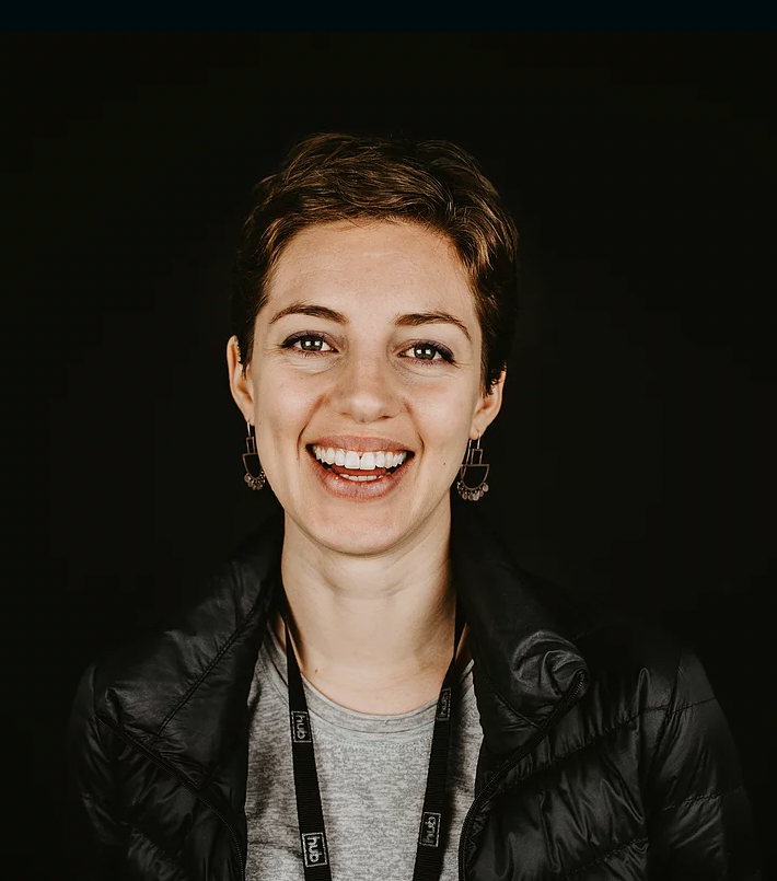 A headshot of a woman smiling, against a black background