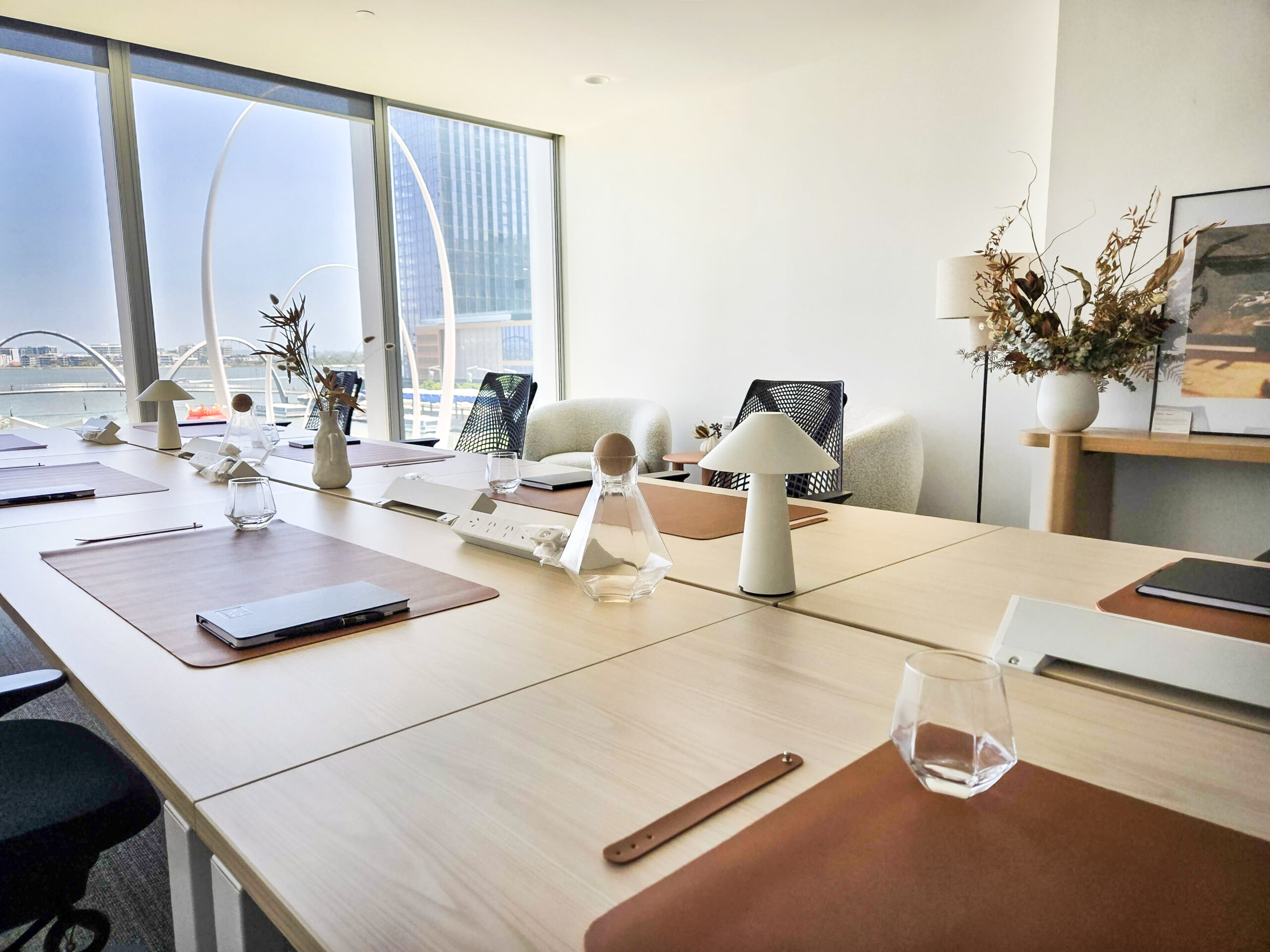 Modern office space with a long shared desk, stylish decor, and large windows overlooking Elizabeth Quay in Perth.