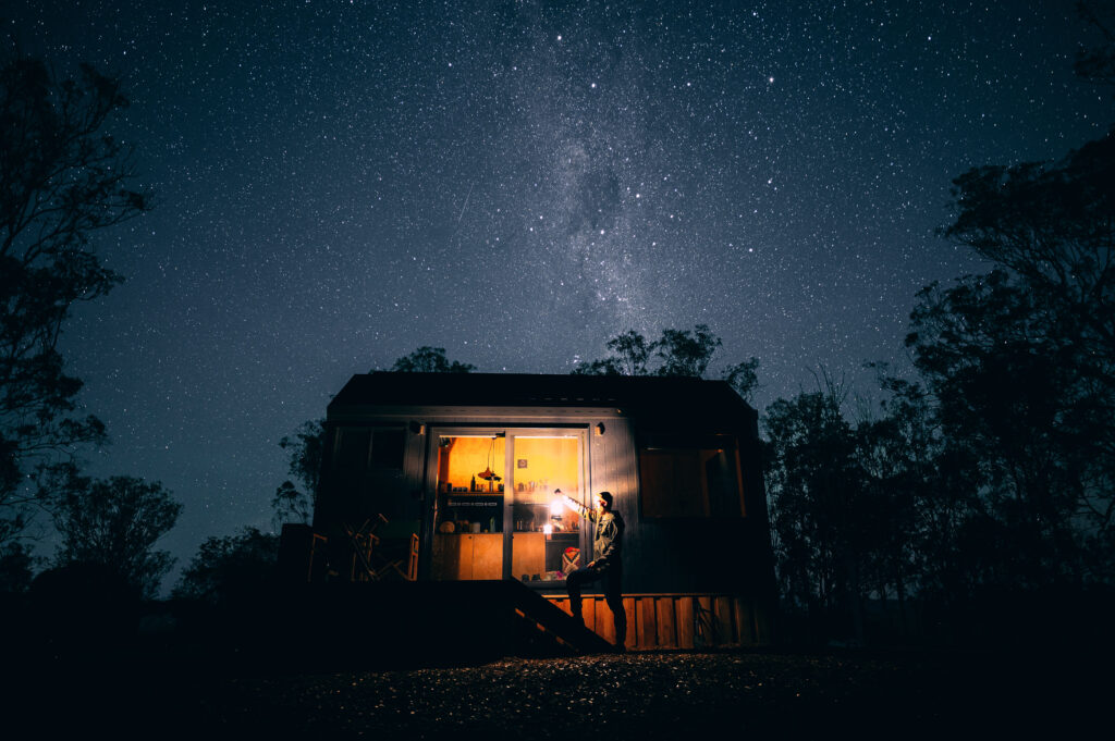 unyoked cabin at night underlooking bright stars with a man holding a lantern admitting light
