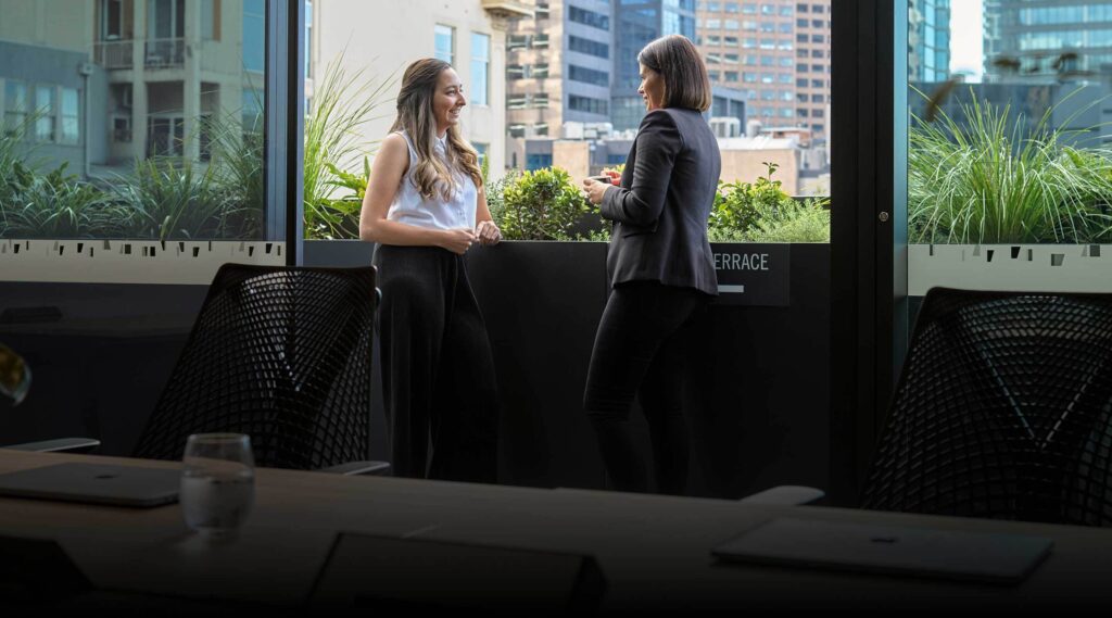 Two professional women engaging in mentorship and conversation on a modern outdoor terrace at Hub Australia.